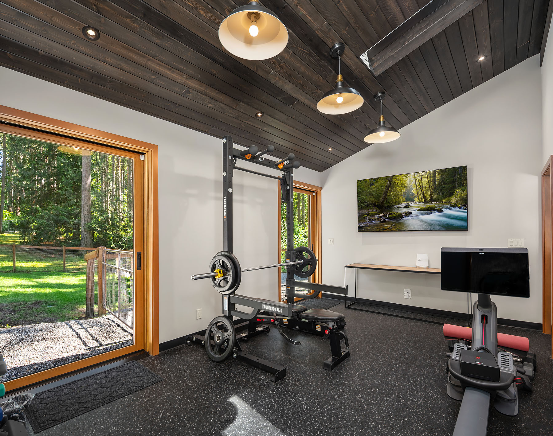 Inside the barn: an exercise room beneath a dark cedar ceiling, nano doors open to the lawn